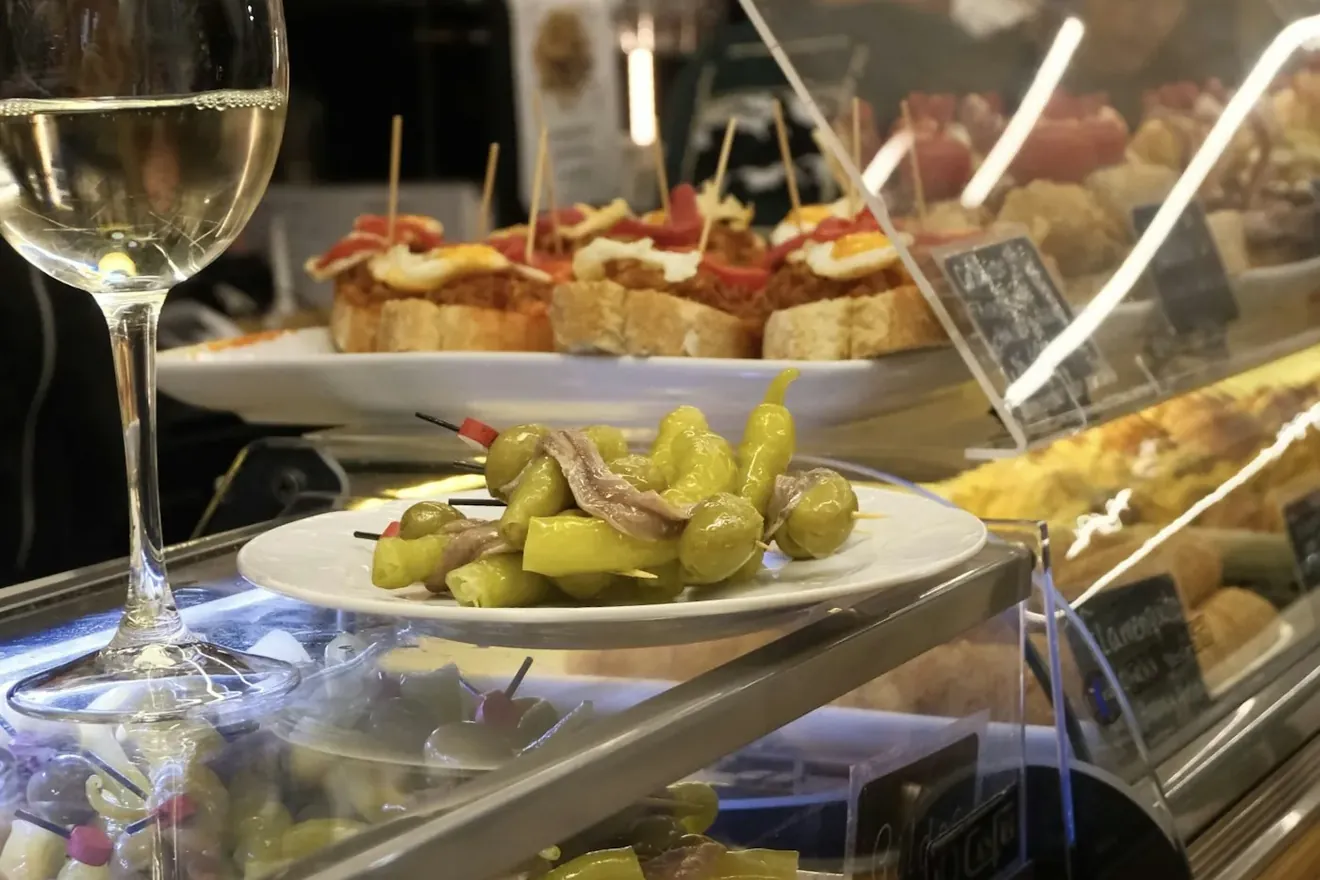 Barra de bar con pinchos y una copa de vino blanco